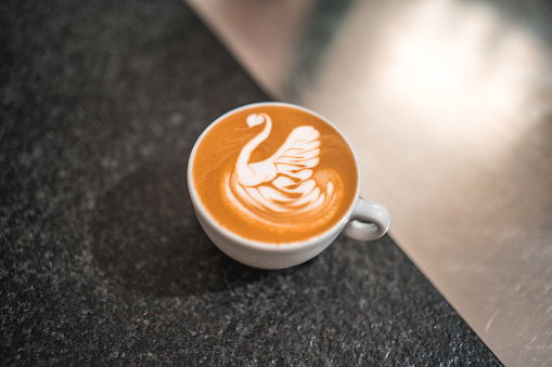 A close-up shot of a coffee cup adorned with stunning latte art, displayed on the bar counter of a cozy coffee house, showcasing the artistry and creativity involved in every sip.