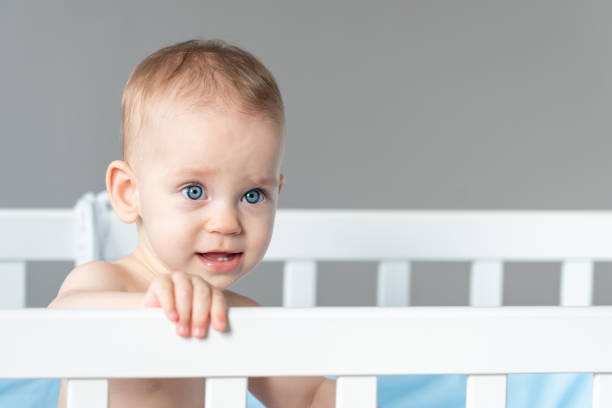istock Baby with a vaguely distorted facial expression in a white classic crib 2118516252