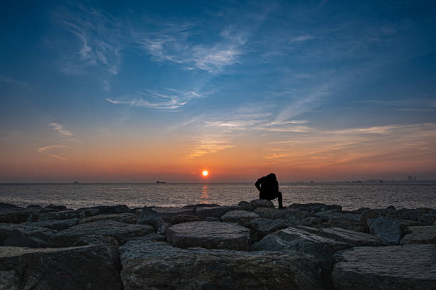 istock Man sitting on the rocks by the sea. sunset. 2118551144