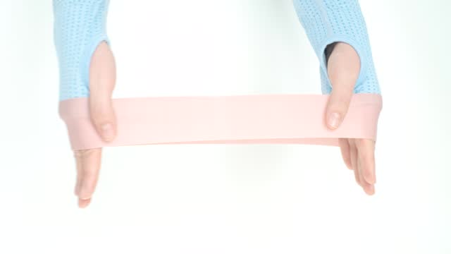 Hands stretching a pink fitness elastic band on white background close-up.