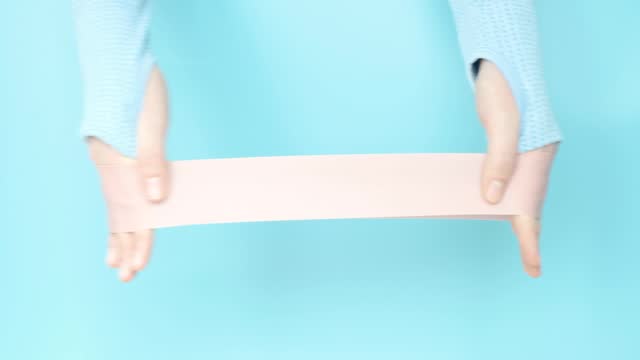 Female hands stretching a pink fitness elastic band on blue background close-up.