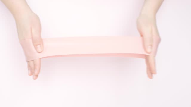 Female hands stretching fitness elastic band on pink background close-up.