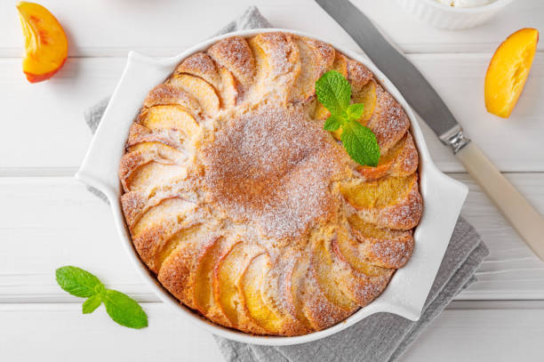 istock Delicious peach pie in a white ceramic baking form on a white wooden background. Summer cake. Selective focus, copy space. 2118783883