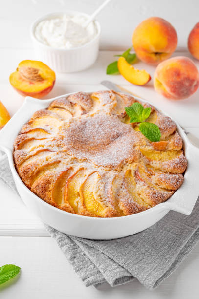 istock Delicious peach pie in a white ceramic baking form on a white wooden background. Summer cake. Selective focus, copy space. 2118783885