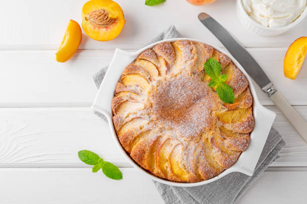 istock Delicious peach pie in a white ceramic baking form on a white wooden background. Summer cake. Selective focus, copy space. 2118783886
