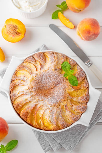 istock Delicious peach pie in a white ceramic baking form on a white wooden background. Summer cake. Selective focus, copy space. 2118783986