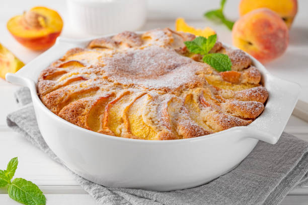 istock Delicious peach pie in a white ceramic baking form on a white wooden background. Summer cake. Selective focus, copy space. 2118784399