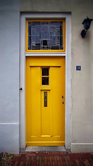 A vertical shot of a modern yellow door from a white building.