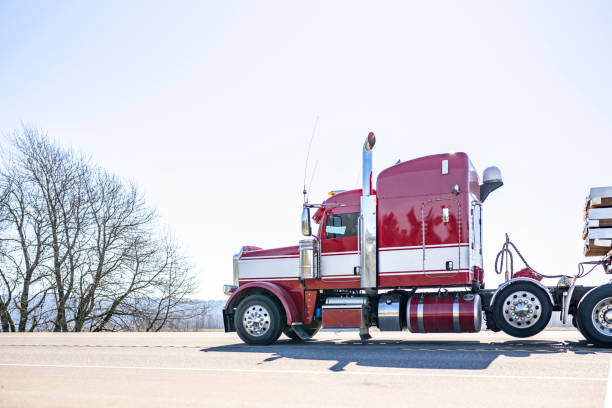 Red big rig classic semi truck with white line on the side transporting cargo on flat bed semi trailer running on the road in sunny day