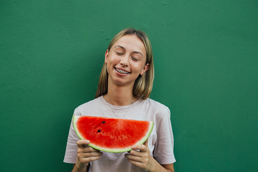 Front view of a cute teenage girl with braces holding a slice of watermelon.