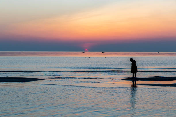 Girl stand near water on seaside on sunset