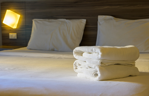 Stack of white towels on bed, ready for use. Soft and fluffy towels neatly folded on top of bedsheet in hotel room
