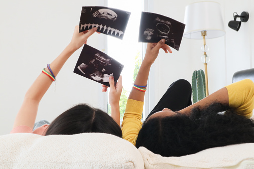 A multiracial lesbian couple lying watching ultrasound images, two lesbians feeling excited about having their first baby by IVF (In vitro fertilization) process. Concept of pregnancy and motherhood