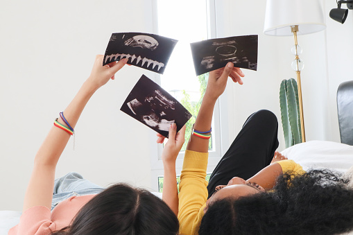 A multiracial lesbian couple lying watching ultrasound images, two lesbians feeling excited about having their first baby by IVF (In vitro fertilization) process. Concept of pregnancy and motherhood