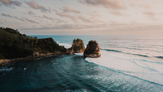 Sunset twilight over natural Sumba Nihisumba Beach with coastal rock formations. Waves from the Indian Ocean splashing towards the natural exotic beach under beautiful sunset twilight at dusk. Aerial Drone Point of View. Sumba Island, Nusa Tenggara Timur, Indonesia, Southeast Asia