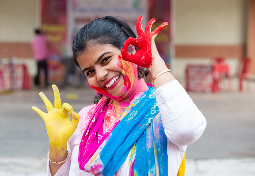 An Indian Bengali woman in white dress and colorful face with powder paint during Holi poses with colorful hands