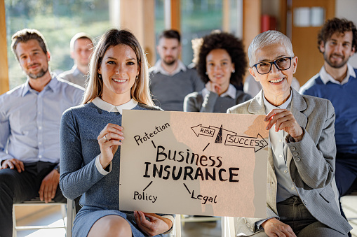 Happy businesswomen holding placard with business insurance strategy during a seminar and looking at camera.