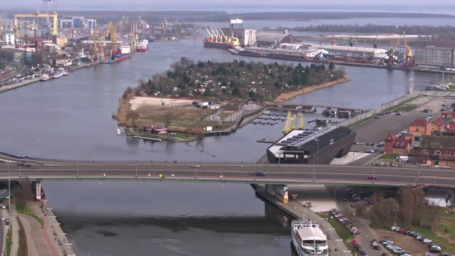 Drone footage over the Oder River in Szczecin on a March day, capturing Szczecin Castle Route, cars, Port of Szczecin, docked ships, cranes, port infrastructure, and Grodzka Island.