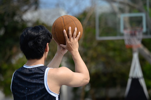 Back view of young basketball player throwing the ball to the basket at outdoor court.
