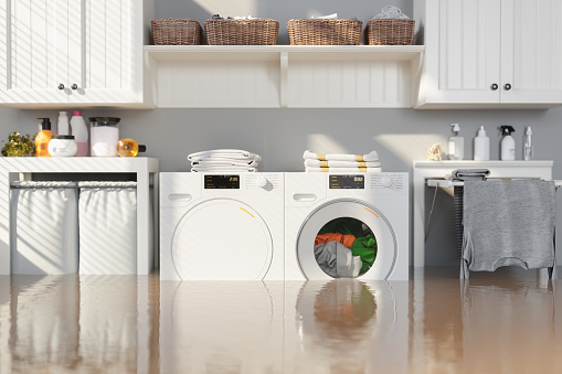 Flooded Laundry Room With Washing Machine, Dryer, White Cabinets and Drying Rack