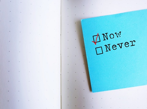 Blue note stick on notebook with text NOW or Never, concept of doing it now, take action to reach goals no more excuses or procrastination and get it done