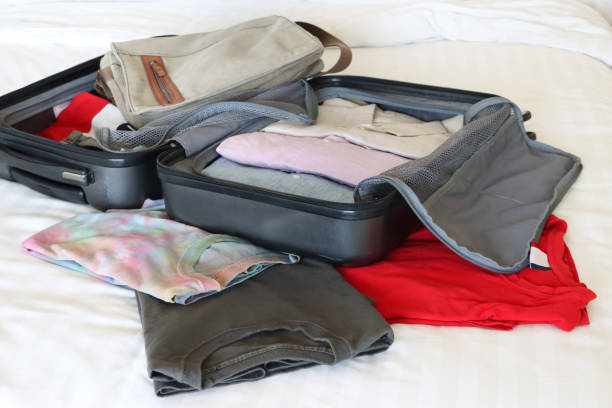 istock Close-up image of open grey wheelie suitcase on double bed, rows of packed folded collared shirts, luggage surrounded by t-shirts, neatly folded clothing, unzipped compartment mesh dividers, beige shoulder bag, focus on foreground 2119186492