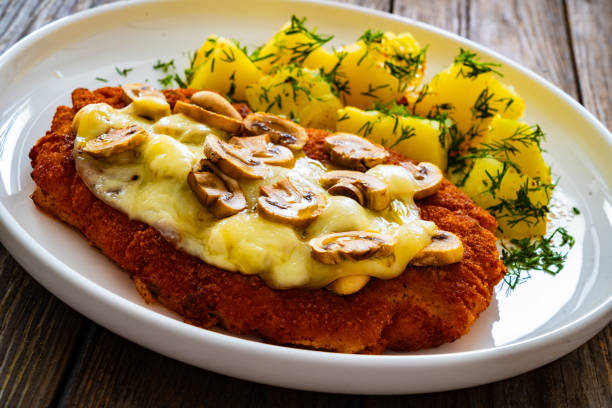 istock Breaded seared chicken cutlet with cheese, white mushrooms and boiled potatoes on wooden table 2119191821
