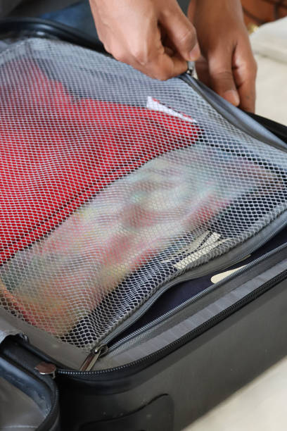 Stock photo showing close-up, elevated view of a grey wheelie suitcase on a double bed mattress covered in fresh bedding. The case has been packed with neatly folded t-shirts.