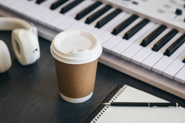 istock Musician workplace table with paper cup and white piano keyboard. 2119201207