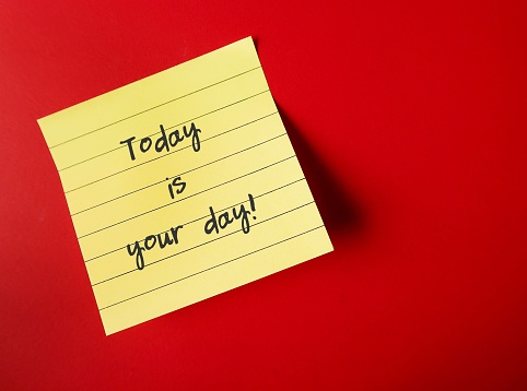 Yellow note on red copy space background with handwriting - TODAY IS YOUR DAY - positive self talk affirmation for self motivation at work