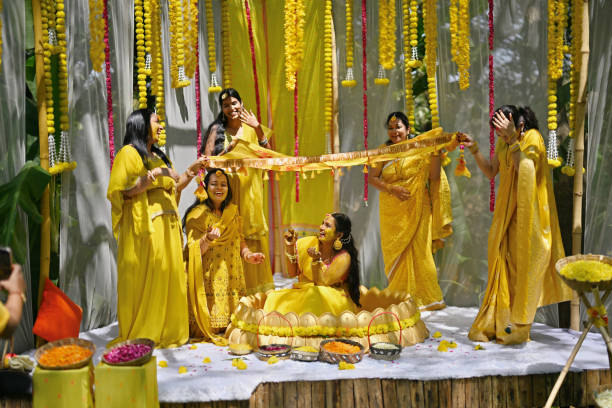 Bride is seated beneath Phoolon ki chadar (flower cover) during her haldi ceremony as a part of the ritual. The bride is seated beneath a Phoolon ki chadar, held up by her friends. Surrounded by loved ones, laughter, and vibrant blooms, the bride basks in the warmth of friendship and the excitement of her upcoming wedding. It's a moment of celebration and camaraderie, as she embraces the festive atmosphere of the occasion. haldi ceremony stock pictures, royalty-free photos & images