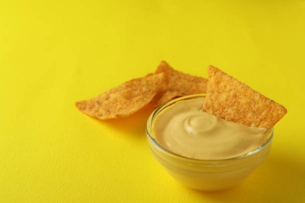 Bowl with cheese sauce and chips on yellow background