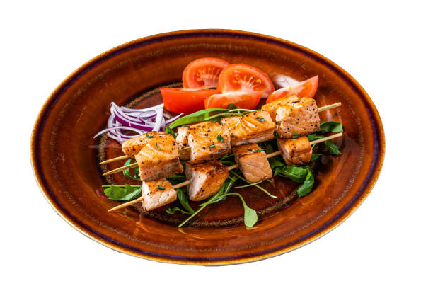 istock Barbecue salmon kebab skewers on rustic plate with vegetables. Isolated on white background. Top view. 2119265911