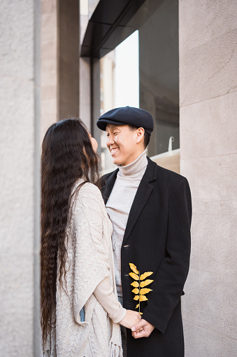 Happy young asian couple in love walking in city, lovers look at each other before kiss. Vertical shot