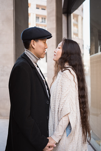 Happy young asian couple in love walking in city, lovers look at each other before kiss