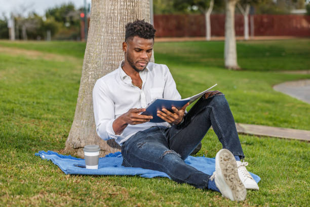 istock Man Relaxing and Reading a Book in the Shade of a Tree 2119284006