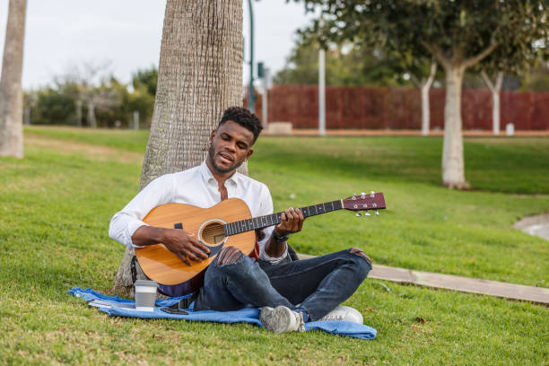 Young man playing acoustic guitar at home, sitting on a comfortable armchair in his living room