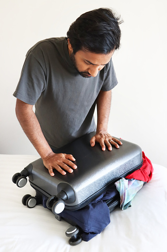 Stock photo showing close-up view of a grey wheelie suitcase on a double bed mattress covered in fresh bedding. The case has been packed with t-shirts.