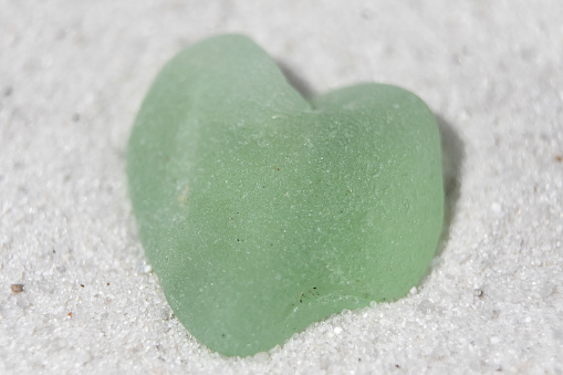 Beautiful sea foam heart shaped beach glass on a sand beach.