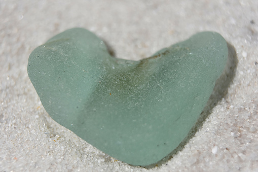 Sea foam heart shaped sea glas on a white sand beach.