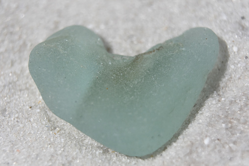 Aqua heart shaped sea glass on a white sand beach.