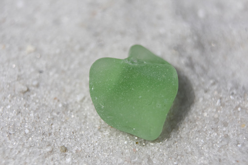 White sand beach with a light green heart shaped sea glass.