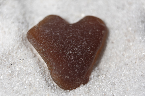 Large brown sea glass in a heart shape on a white sand beach.