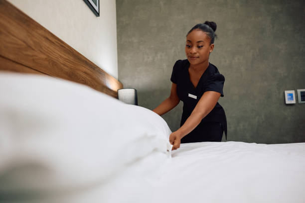 istock Smiling black chambermaid making bed while working in a hotel. 2119364492