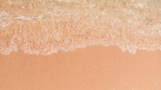 Soft wave edges hitting sandy beach with clear water, in natural daylight. Copy space close up sales ads background.