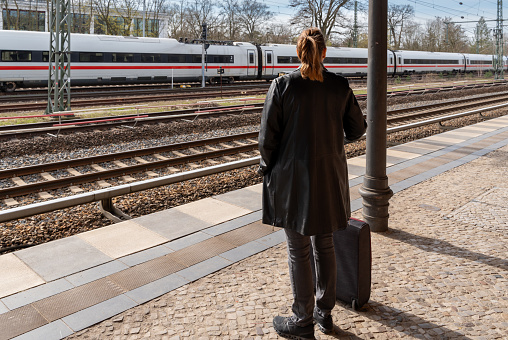 Germany, Berlin, Mars 26, 2024 - Rear view of woman waiting with luggage at railroad station, Berlin Grunewald station