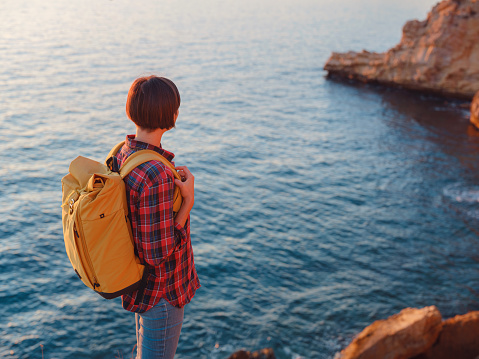 Young woman hiking on rocky beach in Spain, Benidorm. Watching the choppy sea and the bay. traveler enjoying freedom in serene nature landscape