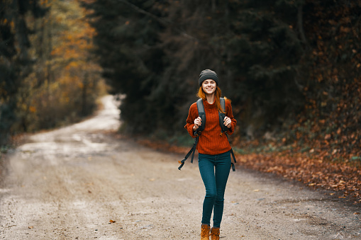 woman with a backpack in full growth walks along the road in the forest . High quality photo