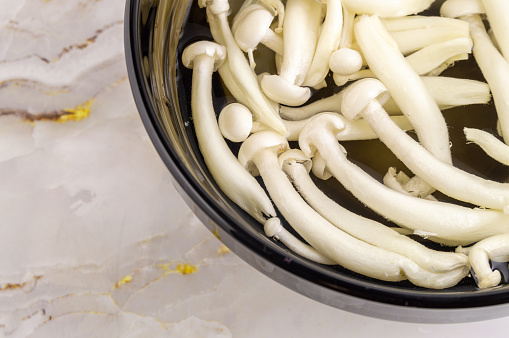 A bowl of mushrooms is sitting on a marble countertop. The mushrooms are white and appear to be fresh