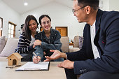 Asian couple looking at house plans and talking with a real estate agent about signing documents for purchase of a new home.